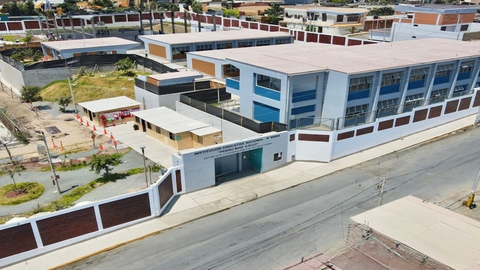 Vista aérea del campus nuevo: pabellones blancos de dos pisos con franjas celestes, cerco perimétrico blanco y ladrillo, patios pavimentados y áreas verdes.