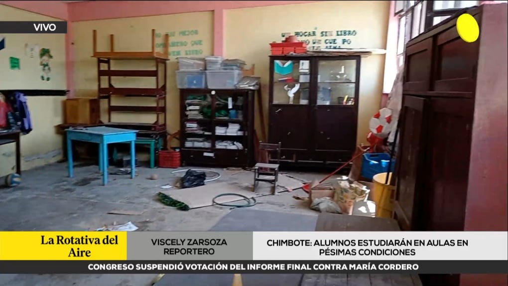 Fotograma televisivo de un aula con muebles arrumbados, paredes rosadas y letreros escolares, durante el reporte de RPP sobre aulas en pésimas condiciones.