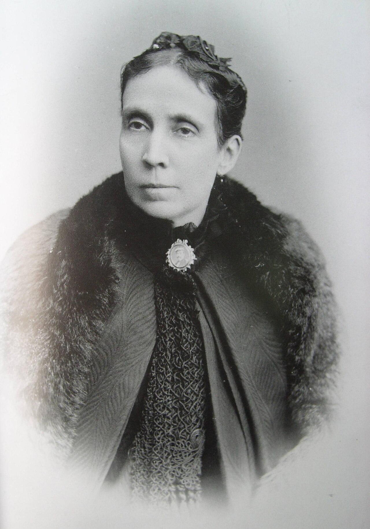 Retrato fotográfico antiguo en blanco y negro de Teresa González de Fanning, con capa de piel y broche con medallón, mirada serena hacia un lado.