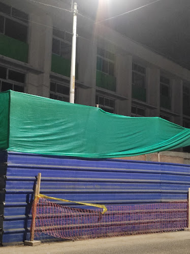 Pabellón del local de la I.E. 89001 visto de noche tras un cerco de obra azul con malla verde, durante el periodo de construcción.