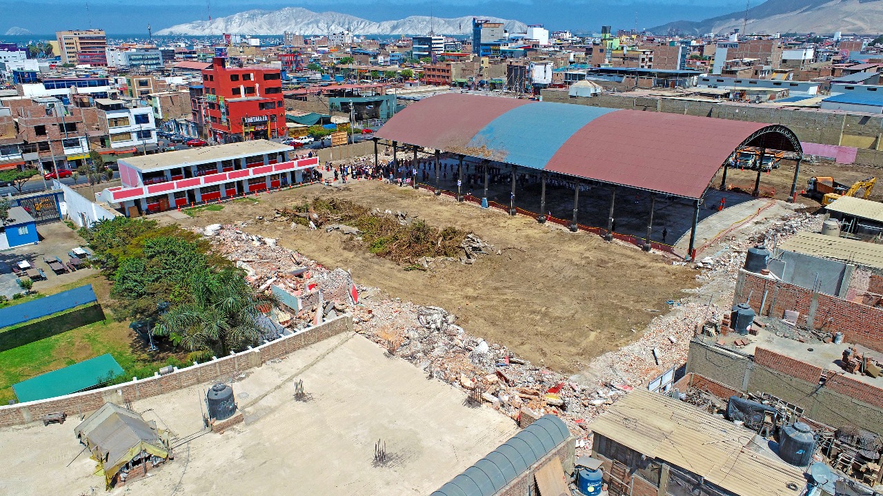 Vista aérea de la manzana escolar con los pabellones antiguos demolidos, escombros y el techo curvo rojo y azul en pie, el día de la ceremonia.