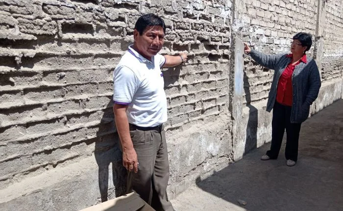 Dos personas observan el muro deteriorado del antiguo local escolar durante la cobertura de julio de 2025.