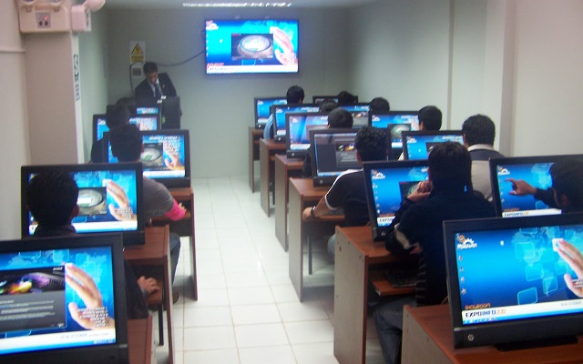 Aula de cómputo del SENATI de Nuevo Chimbote con estudiantes frente a estaciones de trabajo e identificador institucional en pantalla.