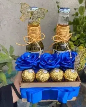 Caja de madera con dos cervezas, rosas azules y Ferrero