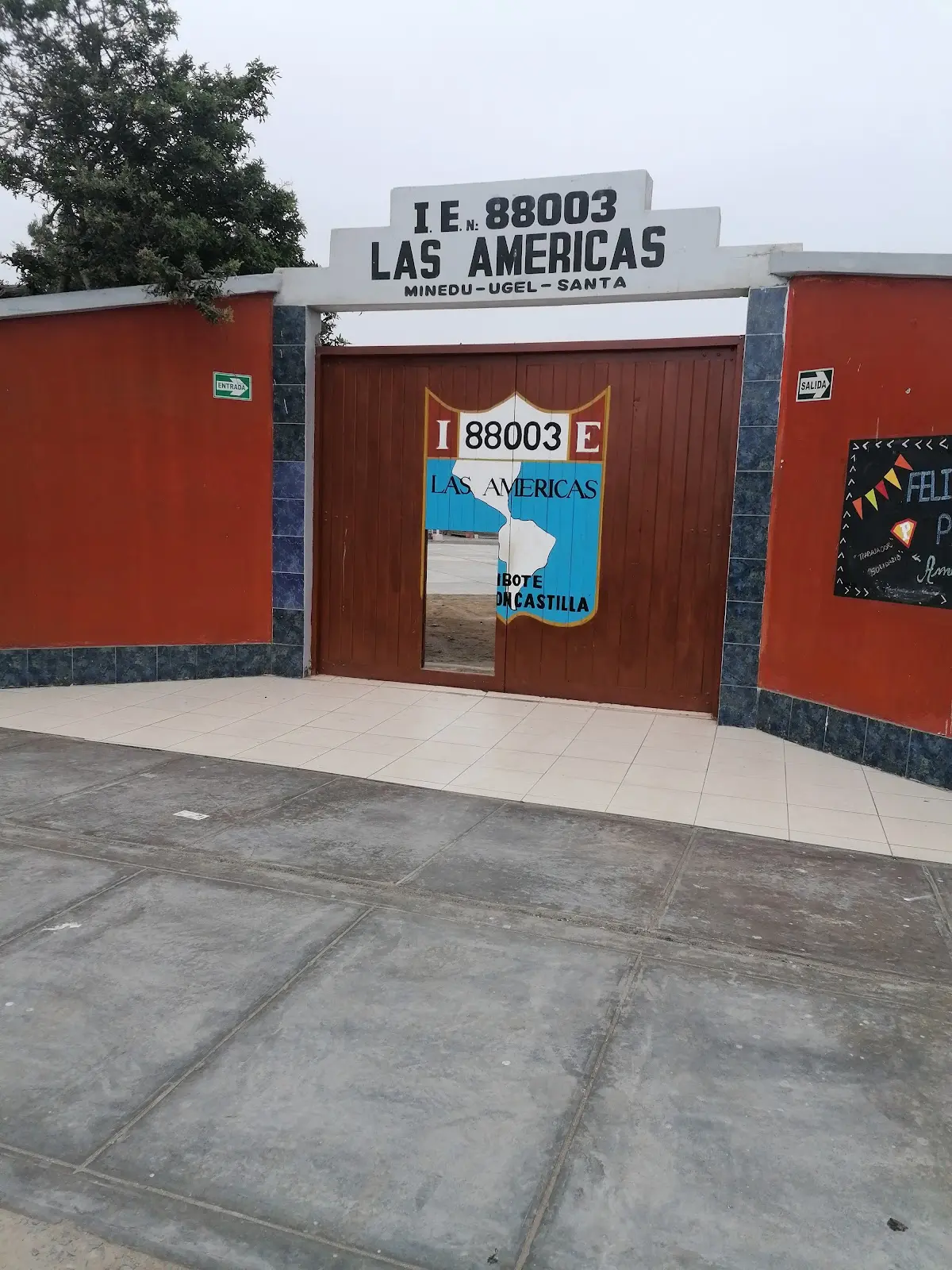 Vista completa del acceso de la I.E. 88003 Las Américas, con rótulo MINEDU UGEL Santa y portón pintado