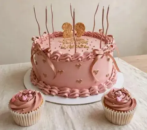 Torta rosa con topper dorado y cupcakes